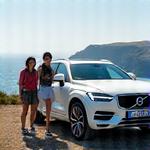 Groupe d'amis riant devant un Volvo XC90 avec un paysage côtier en arrière-plan